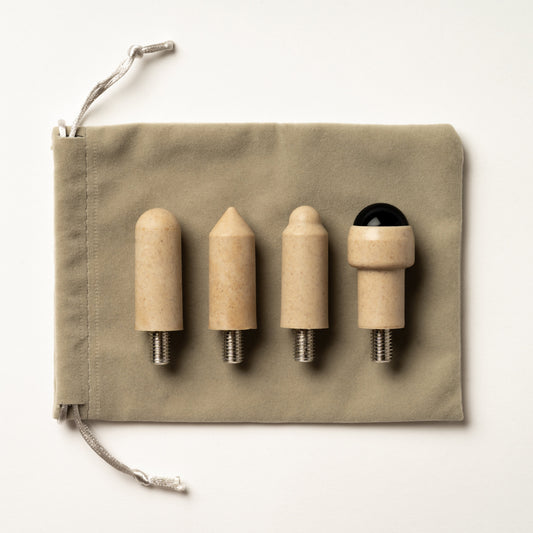 Four beige pegs for the Reliefball or Reliefboard cylindrical tool handles with metal threaded bases are arranged on a muted olive drawstring pouch against a clean white background. One handle has a black spherical end.
