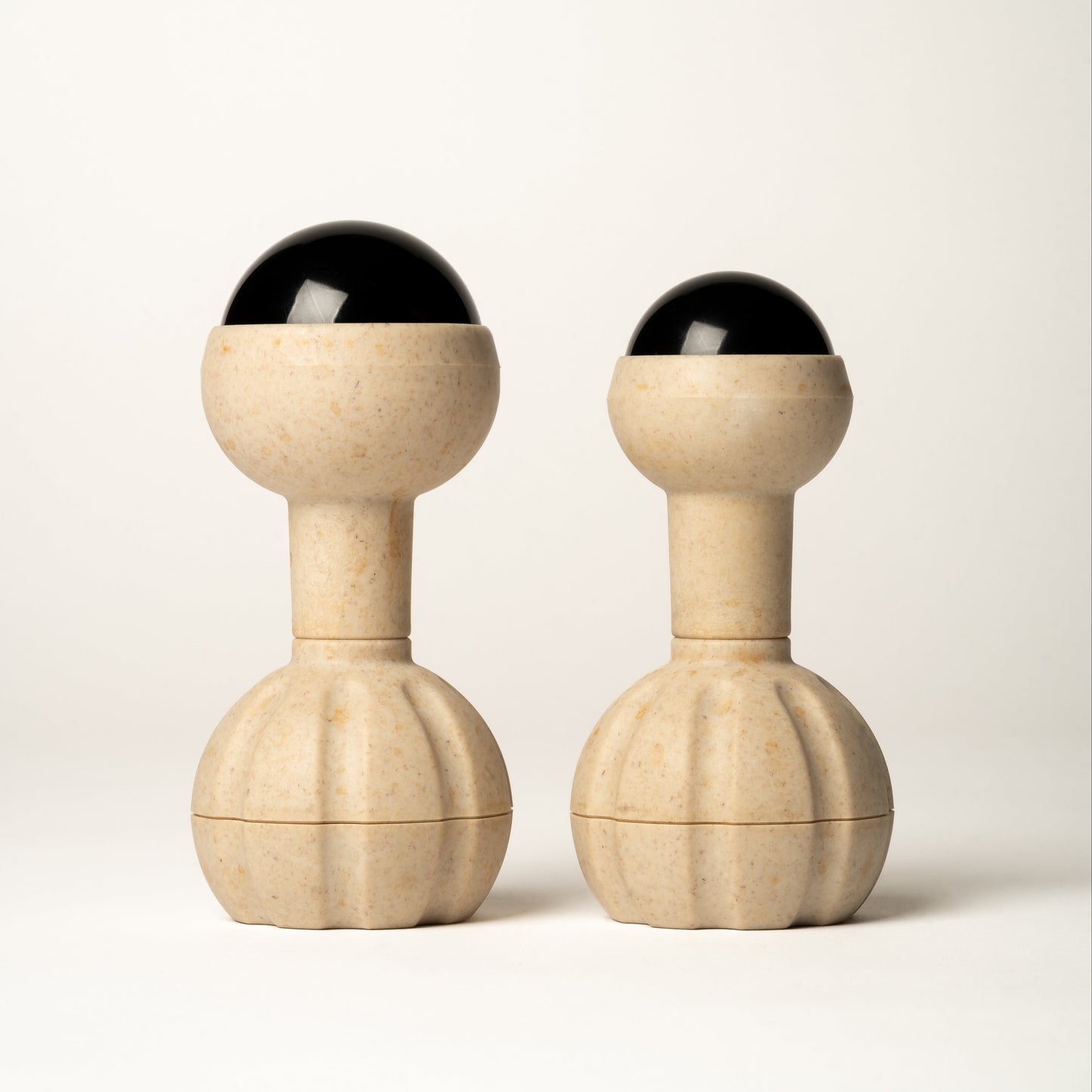 Two matching massage tools with round handles, cylindrical necks, rounded upper sections, and black rollerball tops, photographed on a clean light gray studio background.