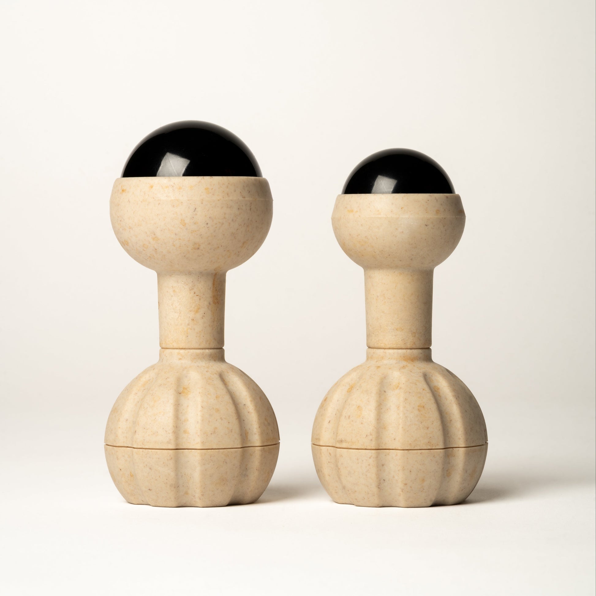 Two matching massage tools with round handles, cylindrical necks, rounded upper sections, and black rollerball tops, photographed on a clean light gray studio background.