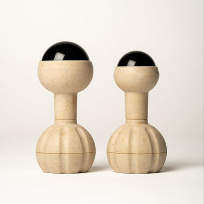 Two matching massage tools with round handles, cylindrical necks, rounded upper sections, and black rollerball tops, photographed on a clean light gray studio background.