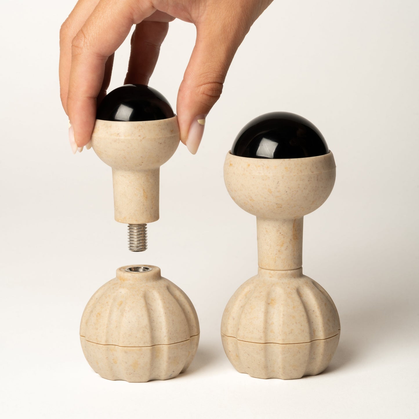 A hand is shown assembling a a rollerball massage head from its handle. Two completed units are displayed on a clean, light off-white background.