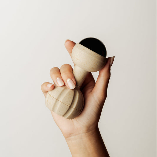 A hand holding a light natural coloured rollerball handheld massager, set against a plain light beige background.